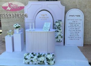 עמדה מעוצבת להפרשת חלה בלבן טהור – שולחן מרכזי אלגנטי עם נרות, כיתוב אישי ולוח תפילה, מוקף פרחים לבנים רכים היוצרים אווירה חגיגית, נשית ומרגשת של קדושה, אחדות וברכה. צילום: לילך
